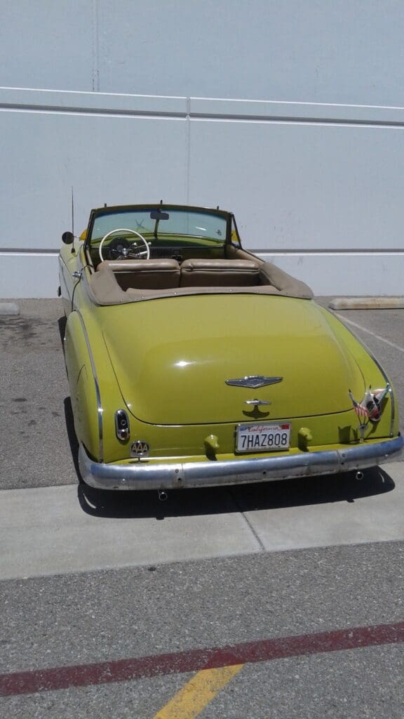 Vintage yellow convertible car parked outdoors under bright sunlight.