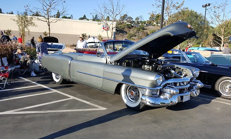 Classic vintage car with hood open at a sunny car show.
