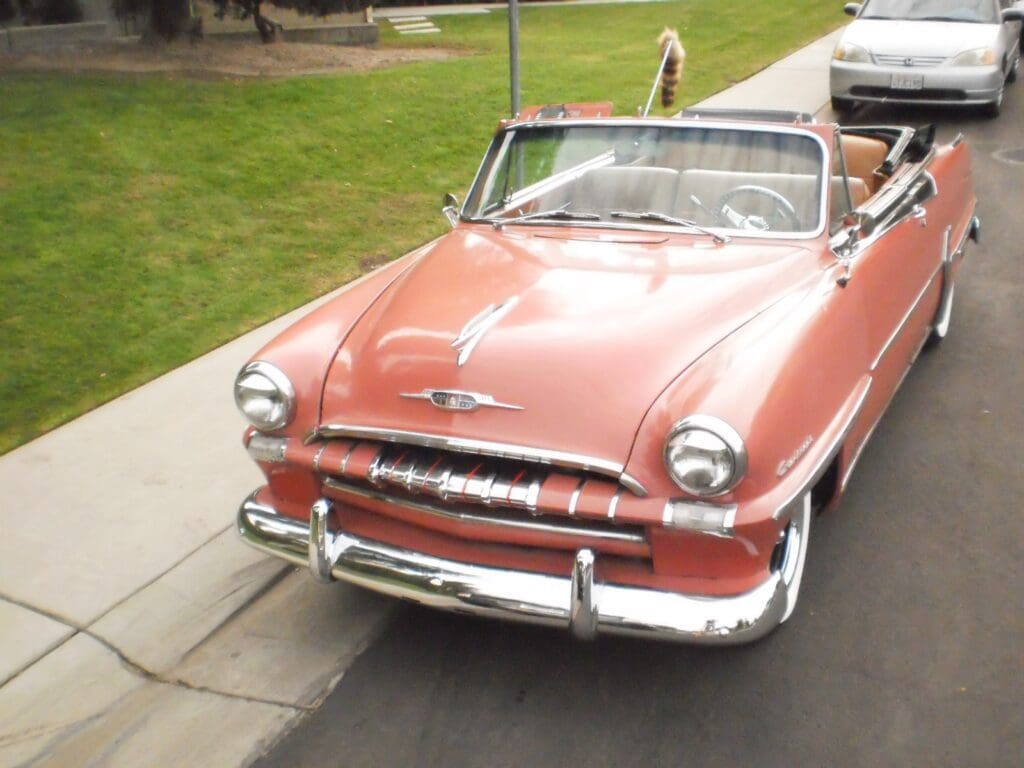 A vintage pink convertible car parked by the curb on a sunny day.