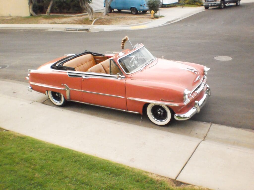 Classic coral-colored convertible car parked on driveway.