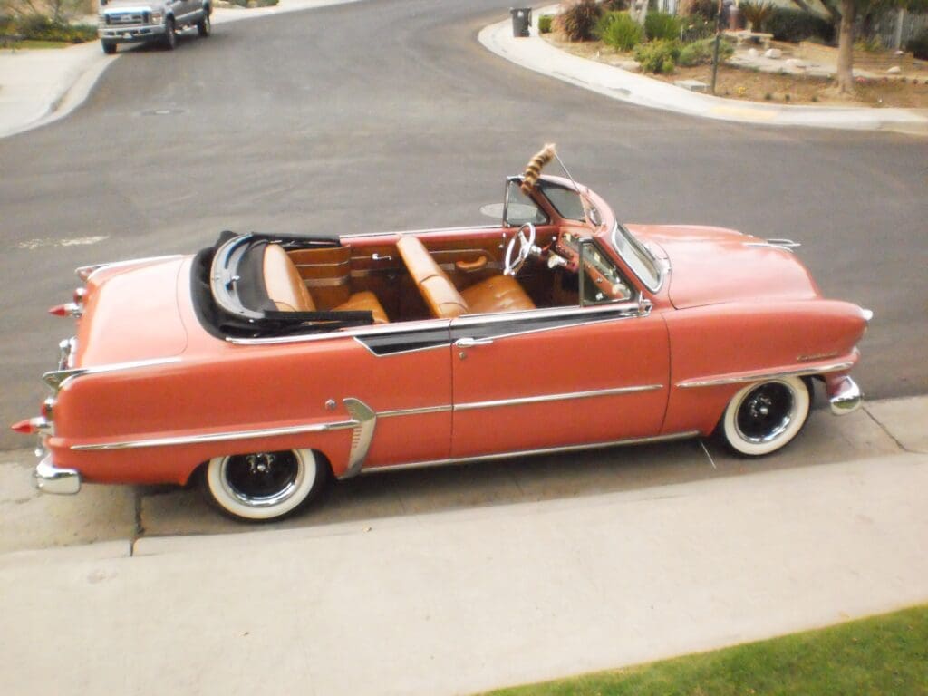 A vintage red convertible car parked on a driveway near a curved road.