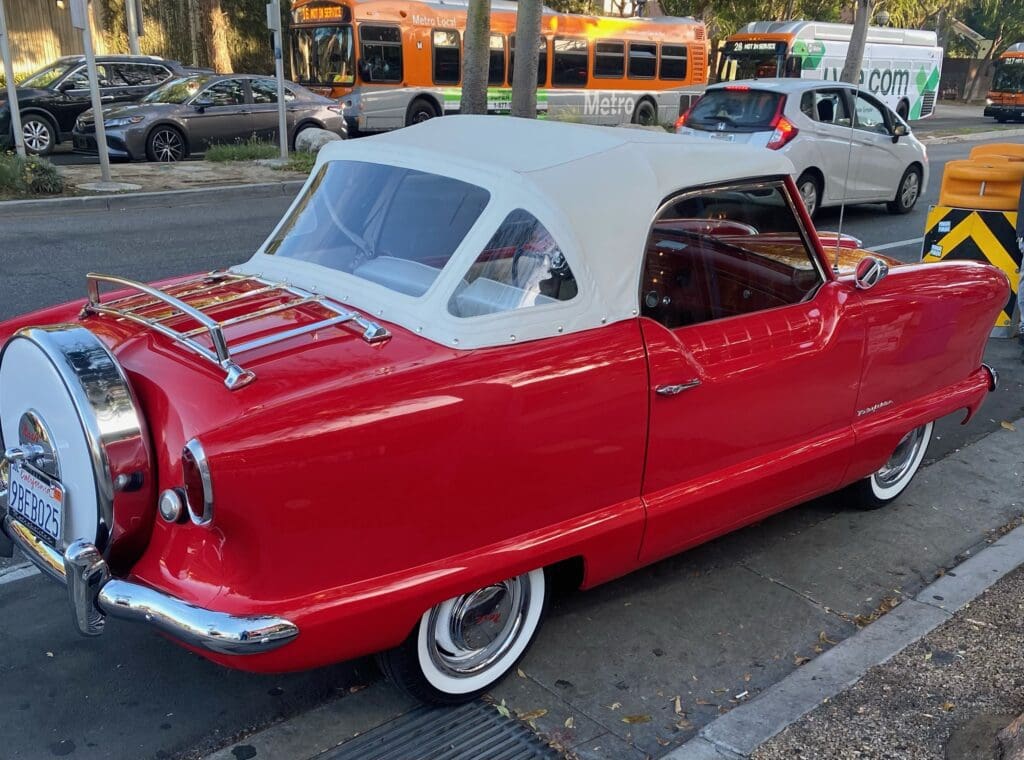 Classic red convertible parked by the seaside under a clear blue sky.