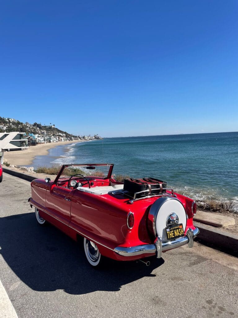 Classic red convertible parked by the seaside under a clear blue sky.