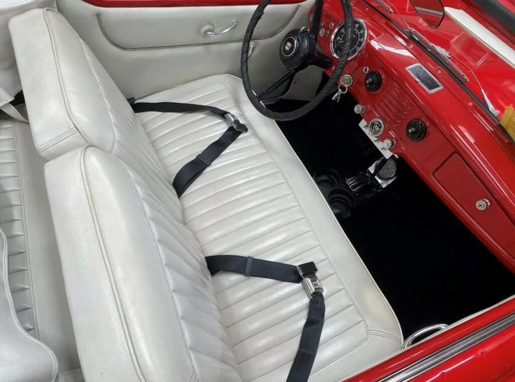 White leather car seats with black seat belts in a vintage red car.