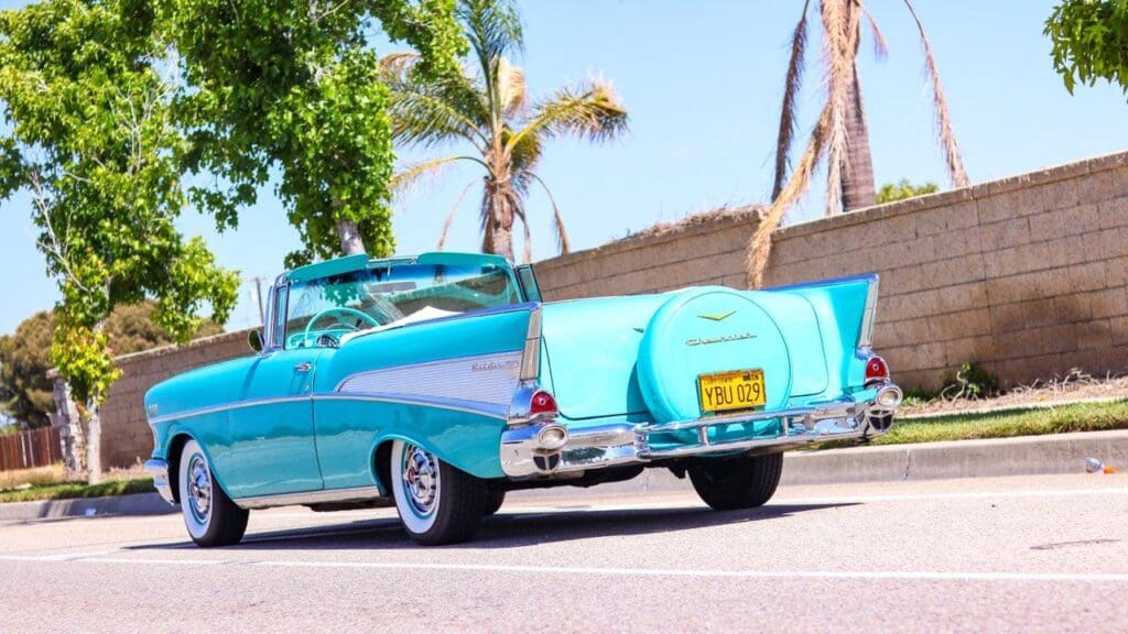 Classic turquoise convertible car parked on a sunny street.