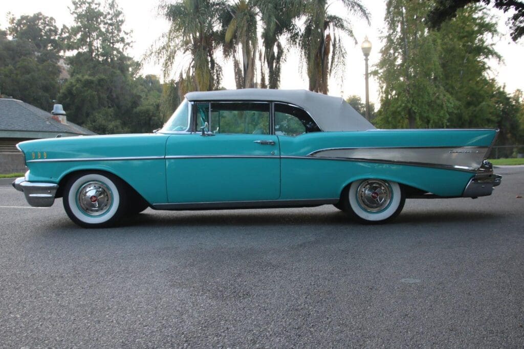 Classic turquoise convertible car parked on a street with palm trees in the background.