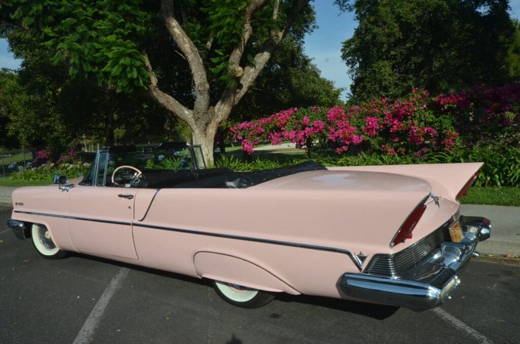 Vintage pink convertible car parked outdoors near trees and flowers.
