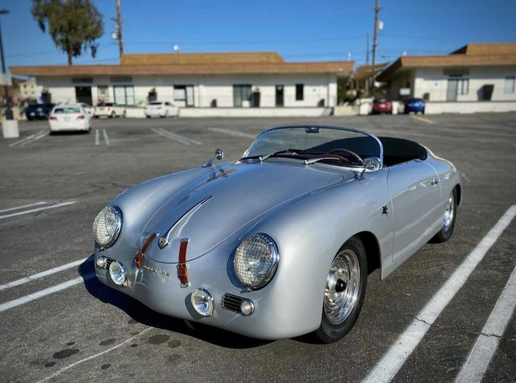 Classic silver Porsche convertible parked in an empty lot under clear blue sky.