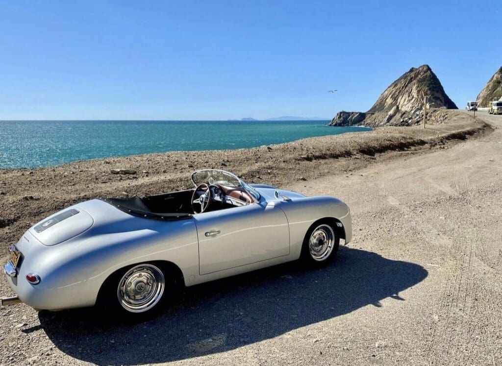 Classic silver convertible parked by a serene beach under clear blue skies.