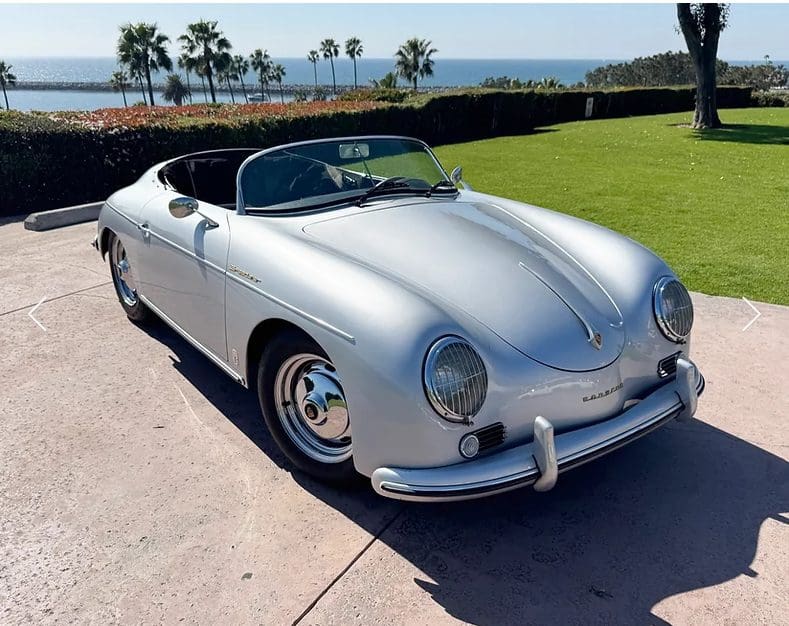 Classic silver convertible car parked near a grassy area by the sea.