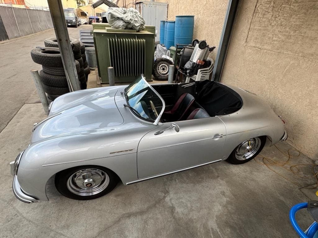A classic silver convertible sports car parked under a covered area.