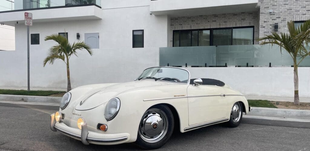 Classic white convertible Porsche parked in front of a modern house.