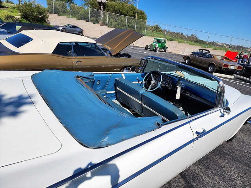 Classic white convertible car with a blue interior parked outdoors on a sunny day.