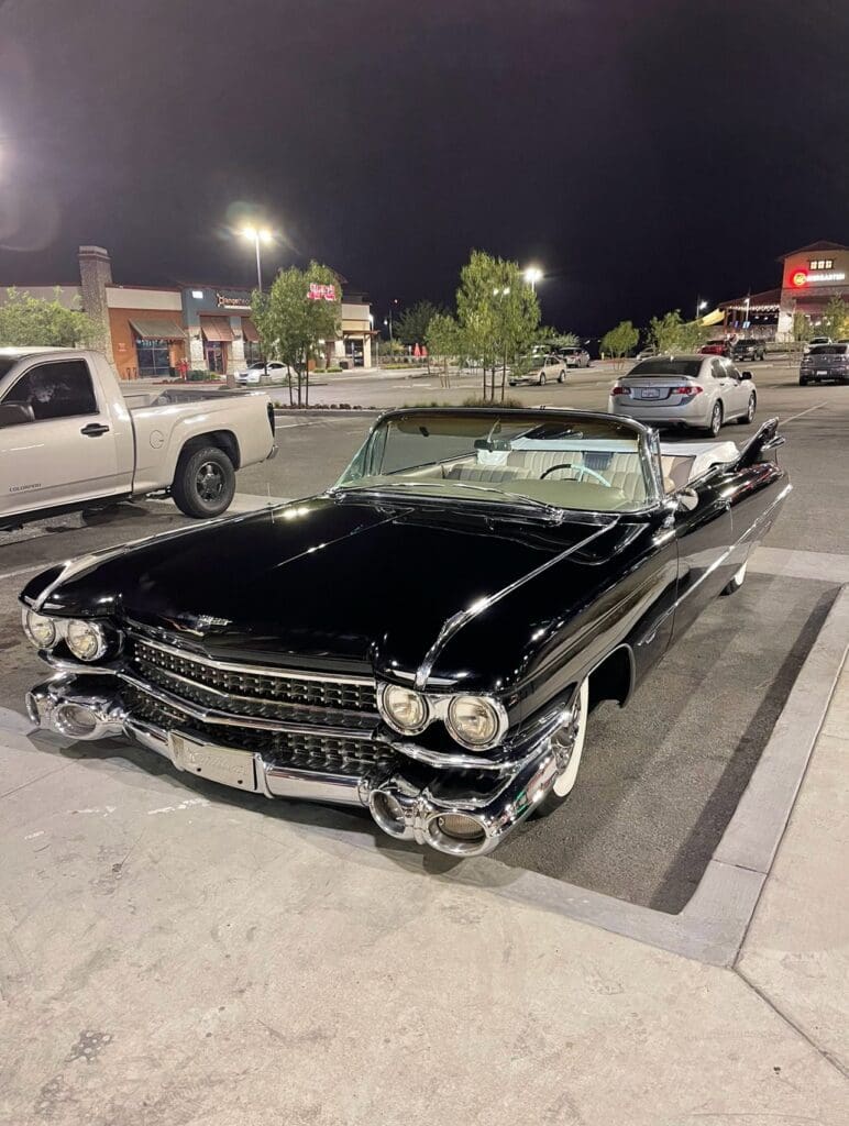 Classic black convertible car parked at night in a parking lot.