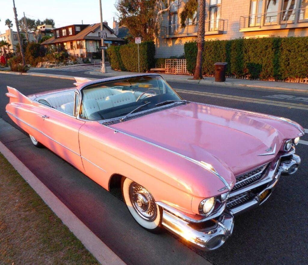 A classic pink convertible car parked on a street at sunset.