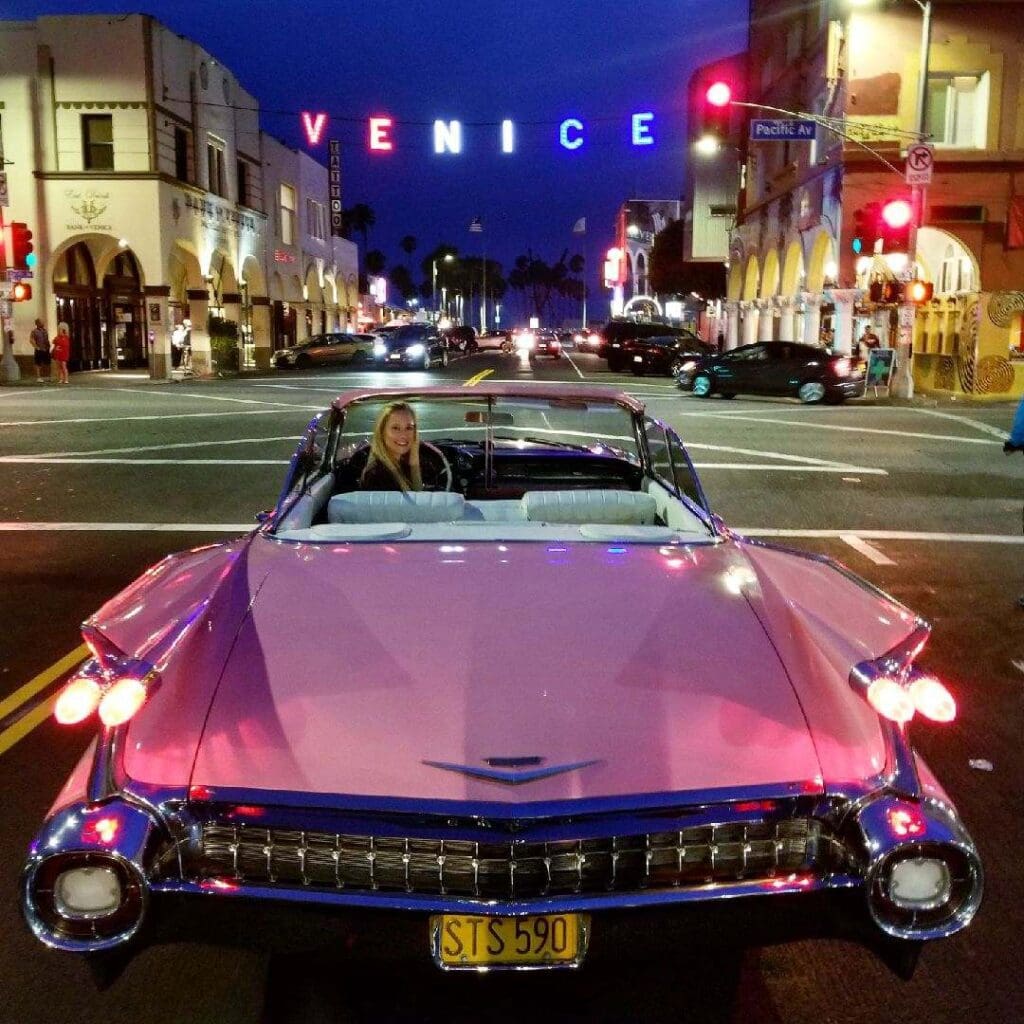 A classic pink convertible car parked on a street at sunset.