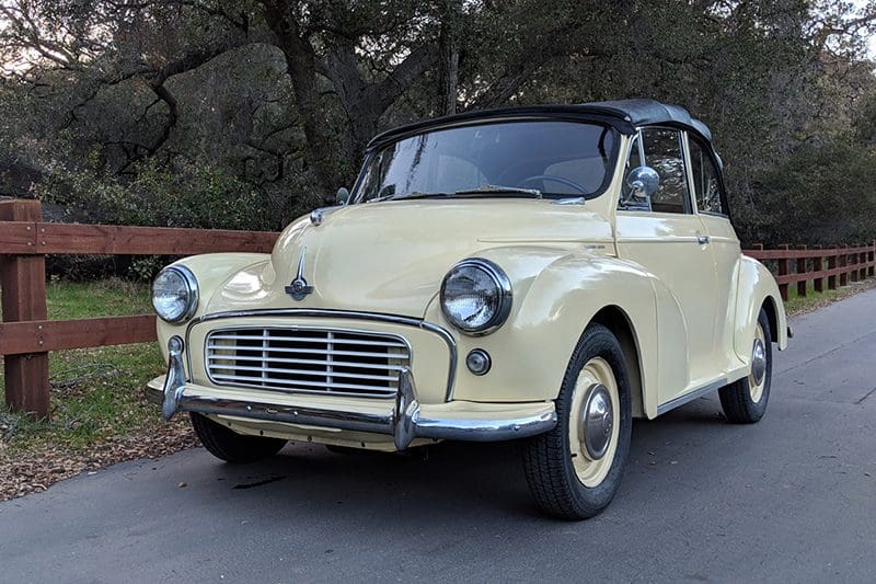 A vintage cream-colored convertible car parked outdoors under trees.