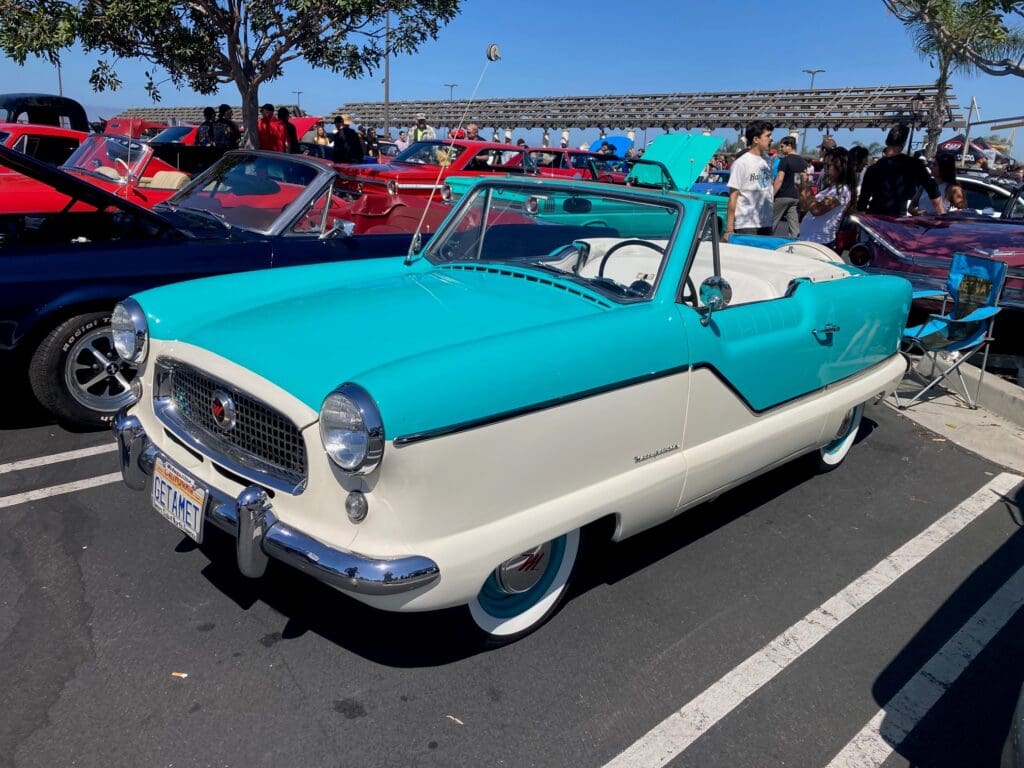 Vintage turquoise and white convertible car at an outdoor car show.