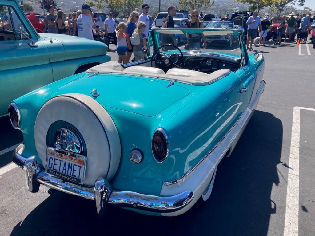 Vintage turquoise and white convertible car at an outdoor car show.