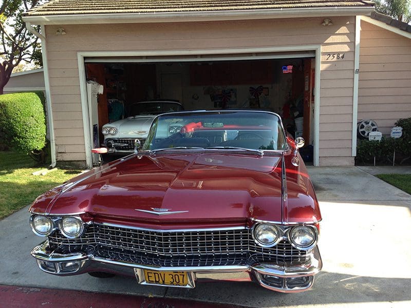Classic red convertible car parked in front of a garage.