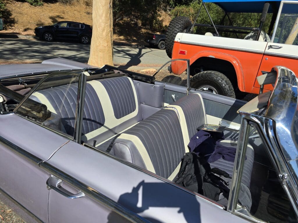 A classic convertible car with black and white seats parked near a vintage orange and white truck.