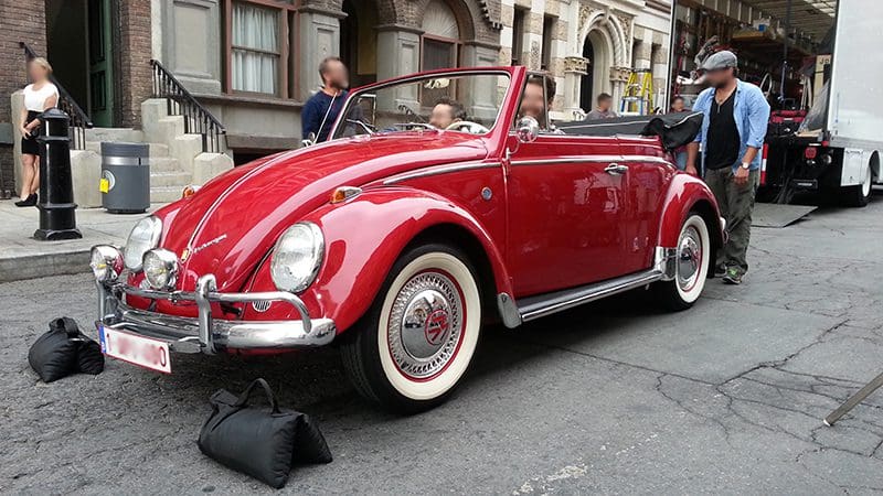 A classic red convertible Volkswagen Beetle parked on a city street.