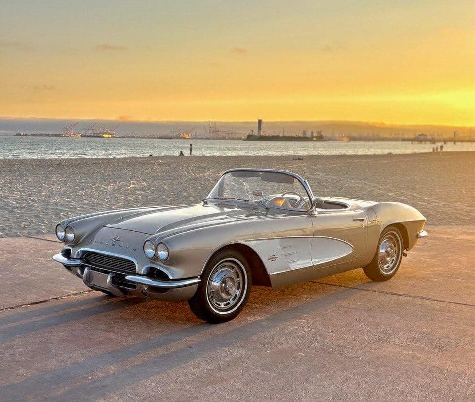 Classic silver convertible car parked by the beach at sunset.