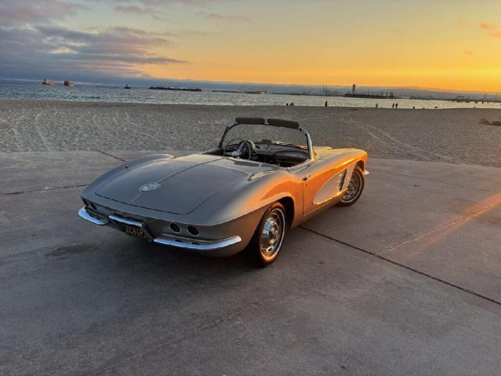 Classic silver Corvette convertible parked by the beach at sunset.
