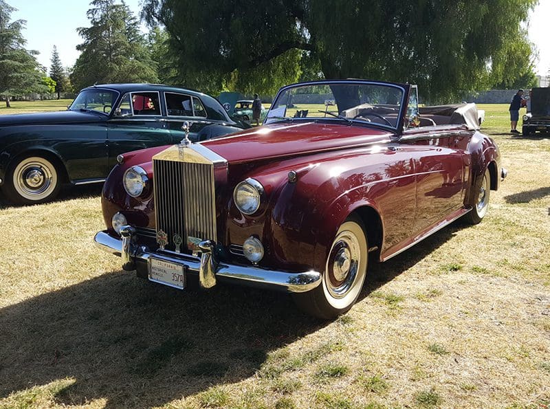 A classic maroon Rolls-Royce convertible parked outdoors on grass.