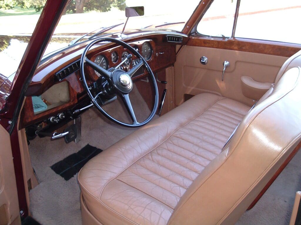 Interior of a vintage car with brown leather seats and wooden dashboard.