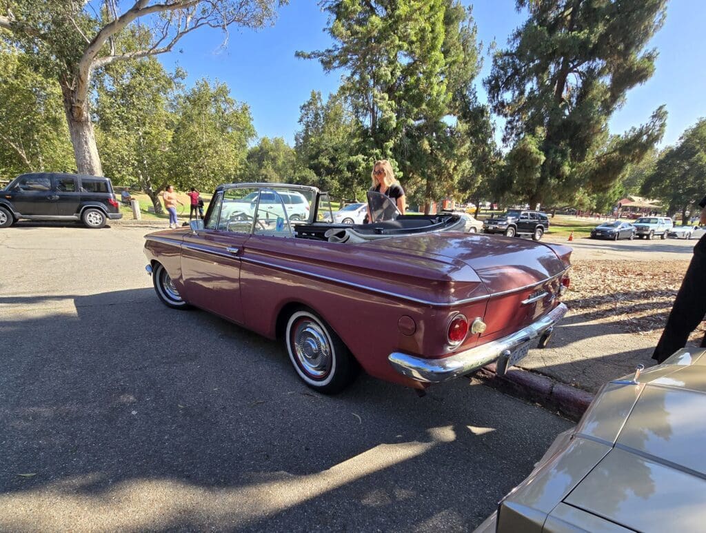 Classic red convertible car parked under trees on a sunny day.
