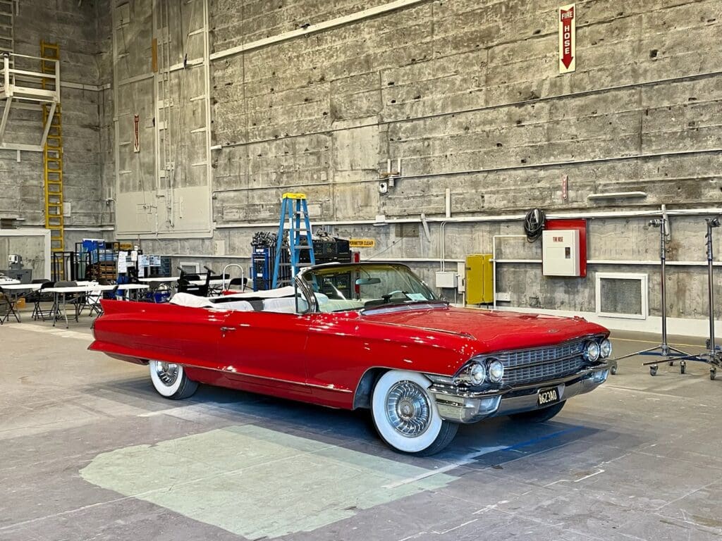 A classic red convertible car with whitewall tires parked indoors.
