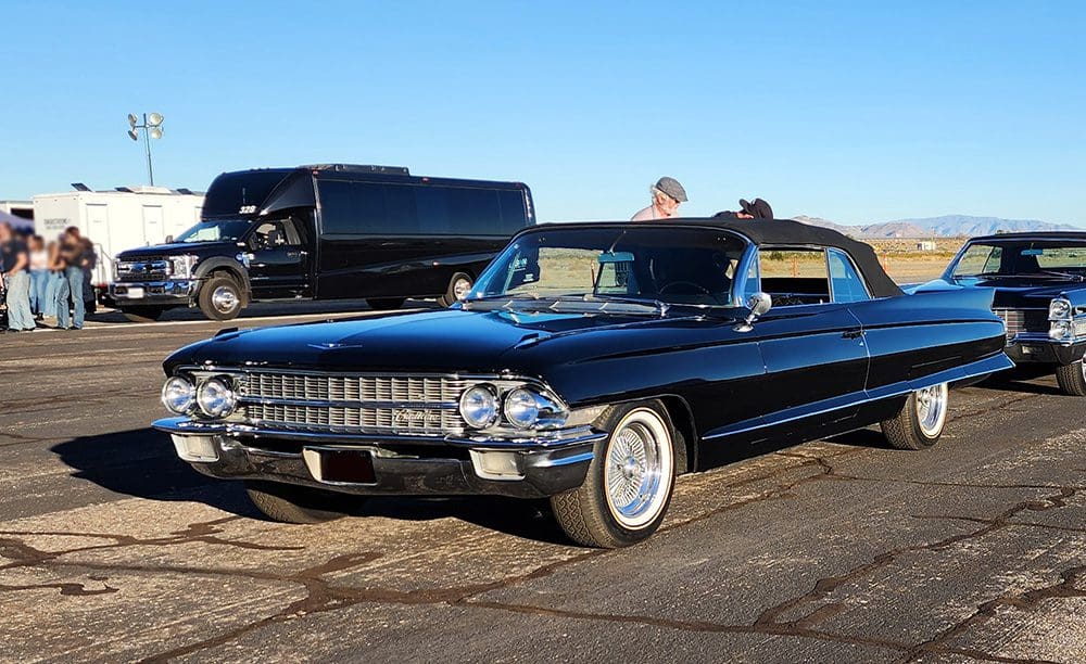 Classic black convertible car parked with people inside, shining under the sun.