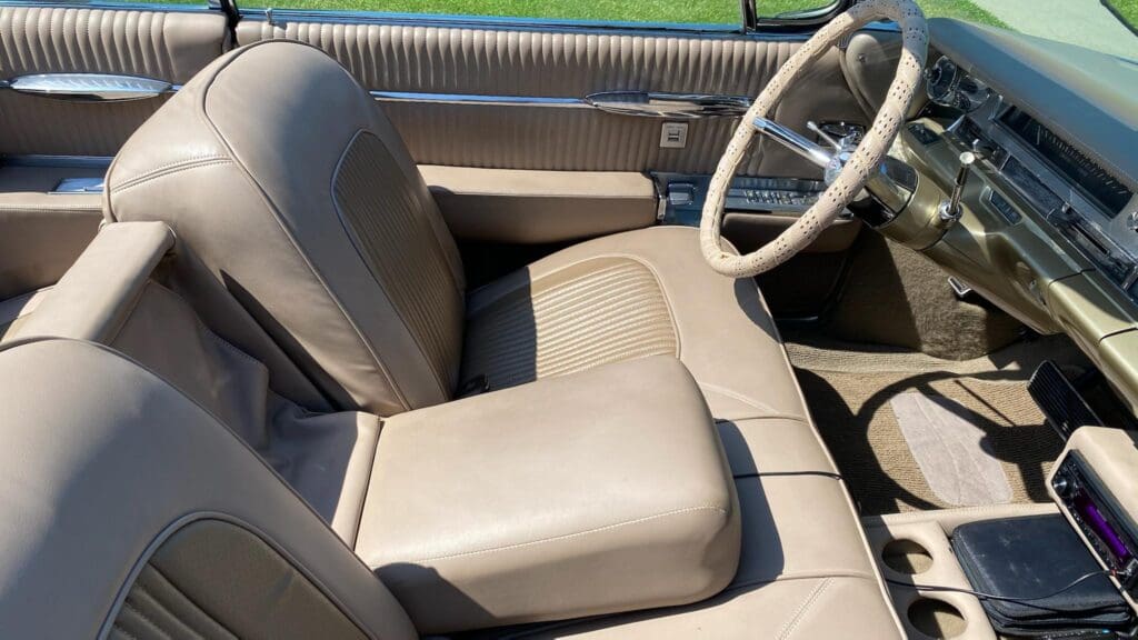 Interior of a vintage car with beige leather seats and a classic steering wheel.