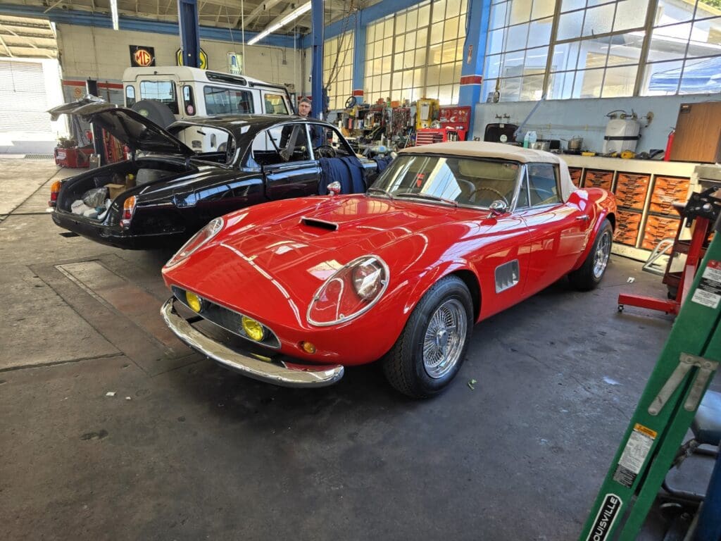 A classic red sports car displayed indoors with other vintage vehicles.
