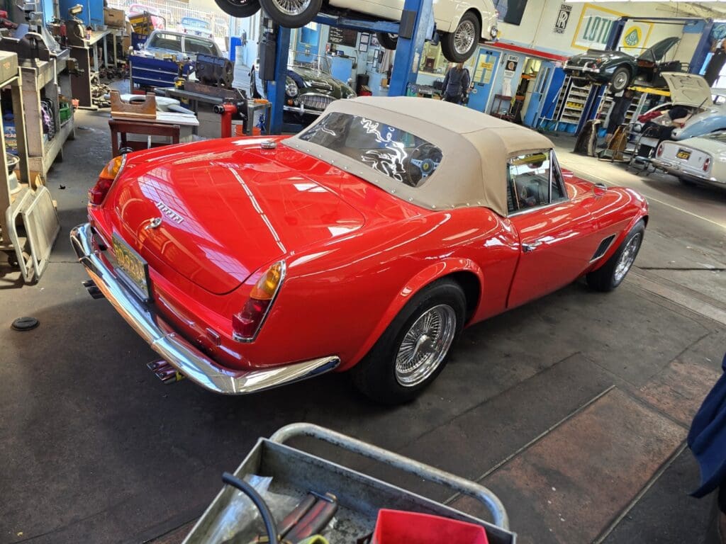 Red vintage convertible car with beige soft top in a workshop.