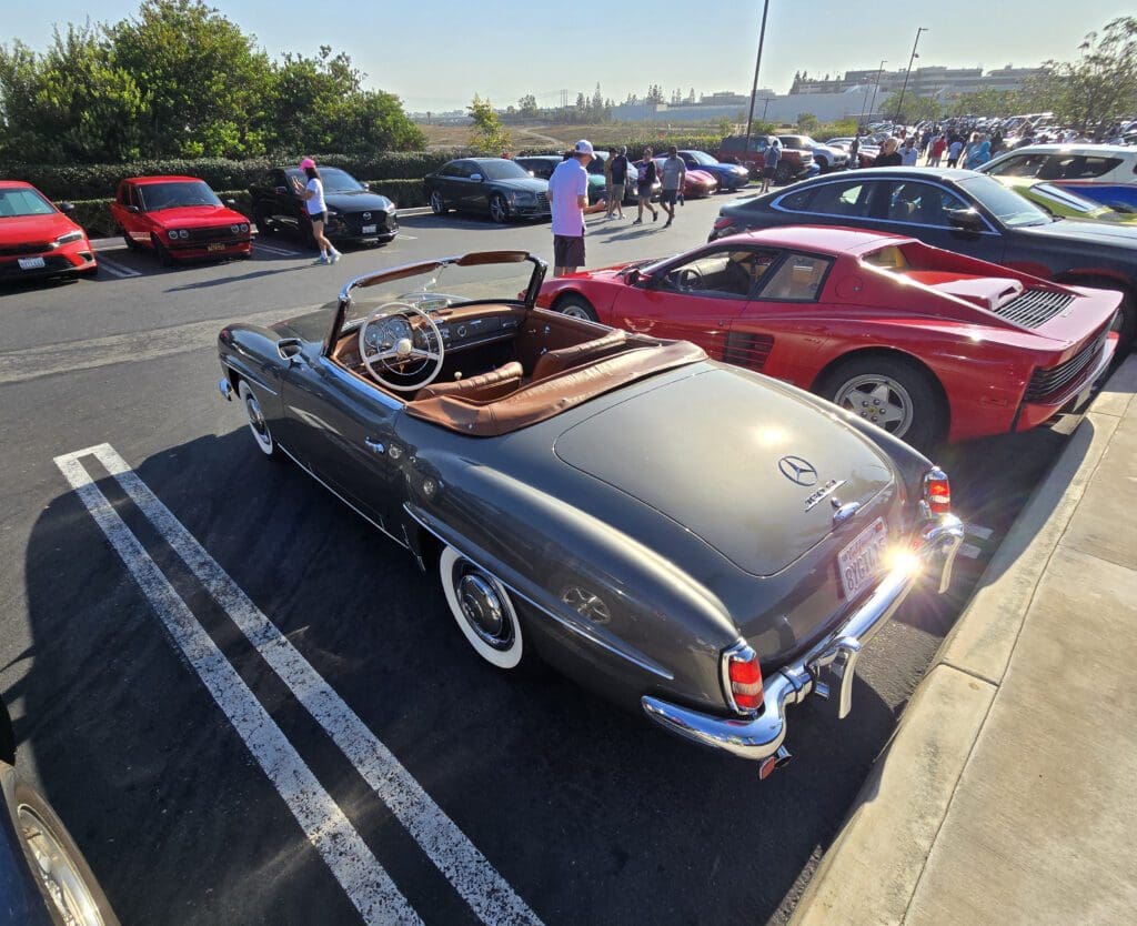 Classic convertible car parked among modern vehicles on a sunny day.