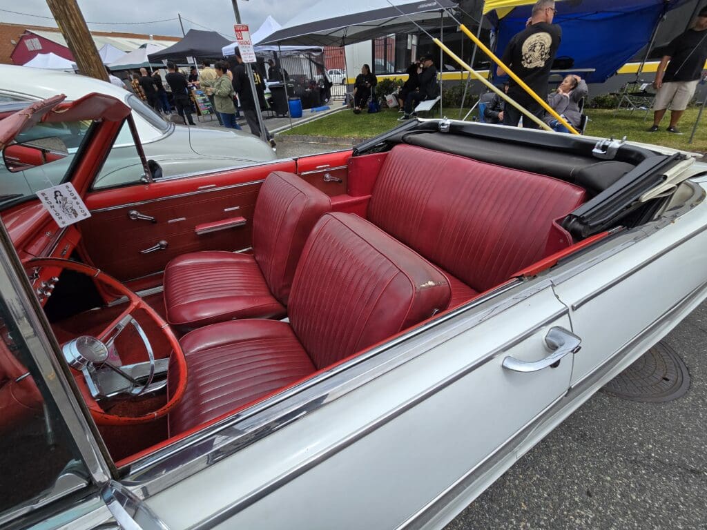 Vintage white convertible car with red leather interior shown at an outdoor event.