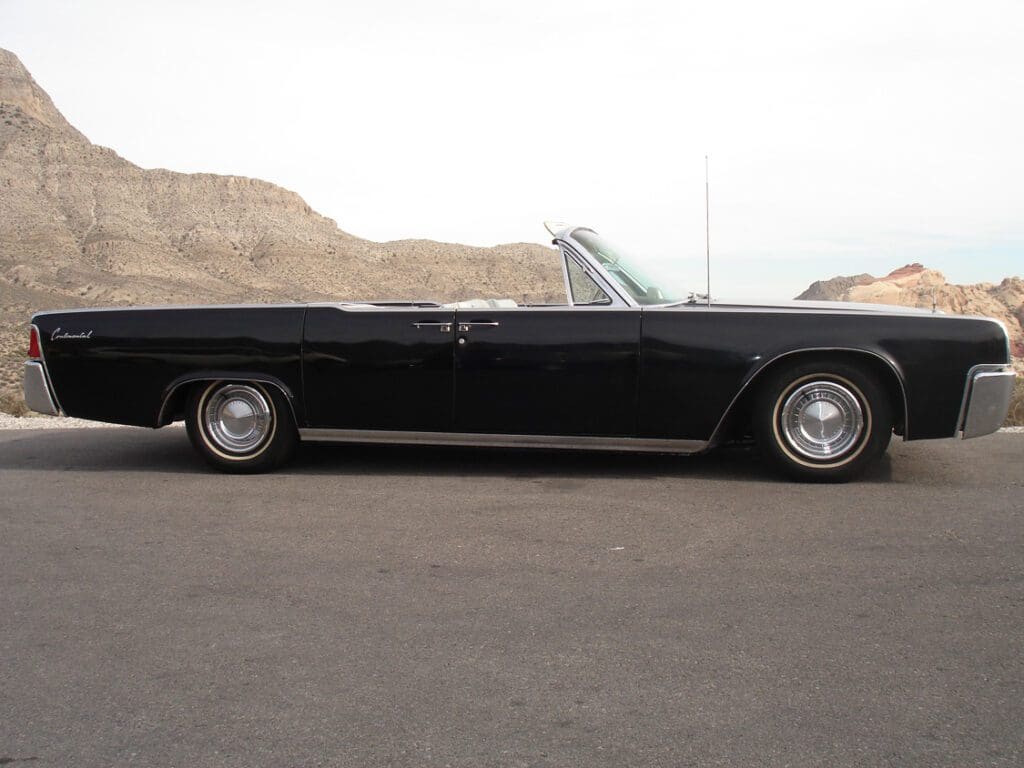 Classic black convertible car parked with desert hills in the background.