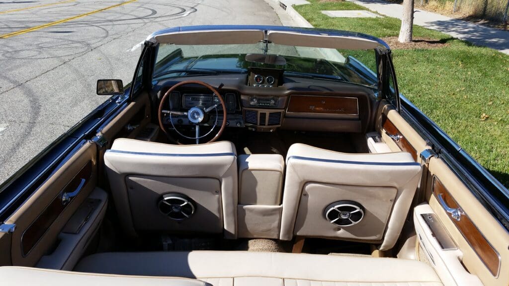 Interior view of a classic convertible car with cream leather seats and wooden dashboard.