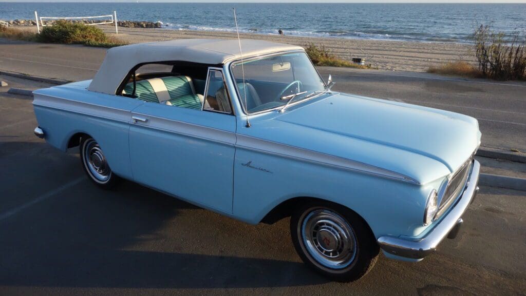 A vintage light blue convertible car parked by the seaside.