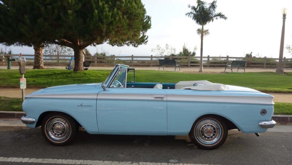 Light blue vintage convertible car parked on a sunny day near a park.