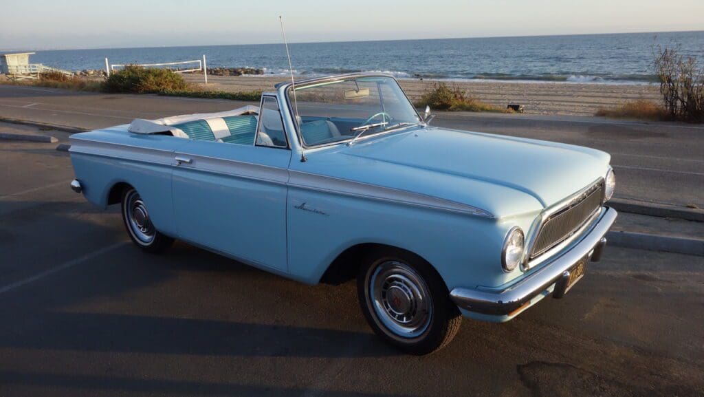 Classic light blue convertible car parked near the ocean.