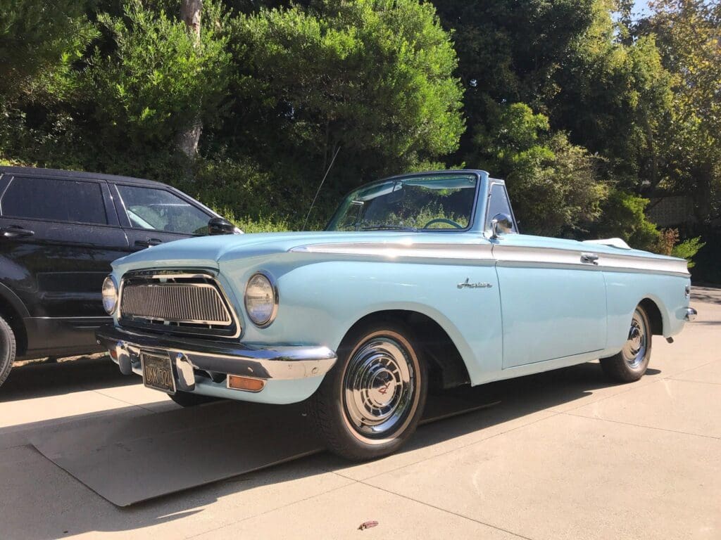 Classic light blue convertible car parked on a sunny driveway.