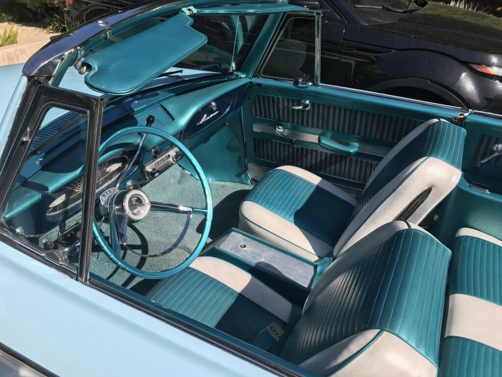 Interior of a vintage car with teal and white seats and steering wheel.