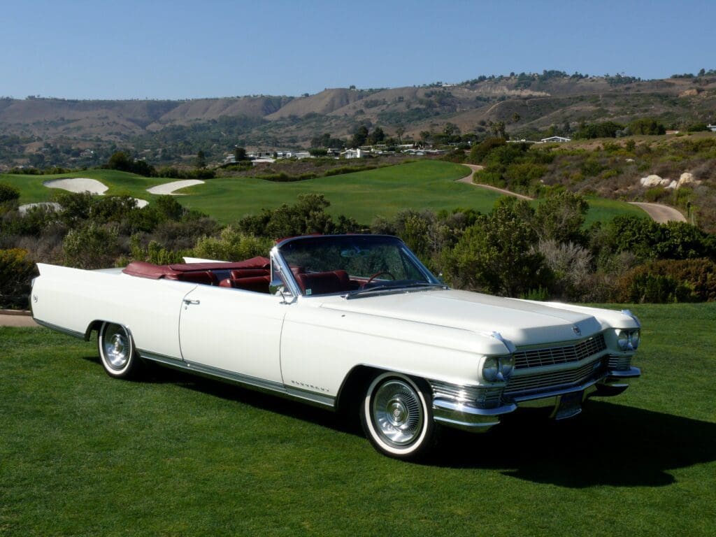Classic white convertible car parked on a green field with hills in the background.