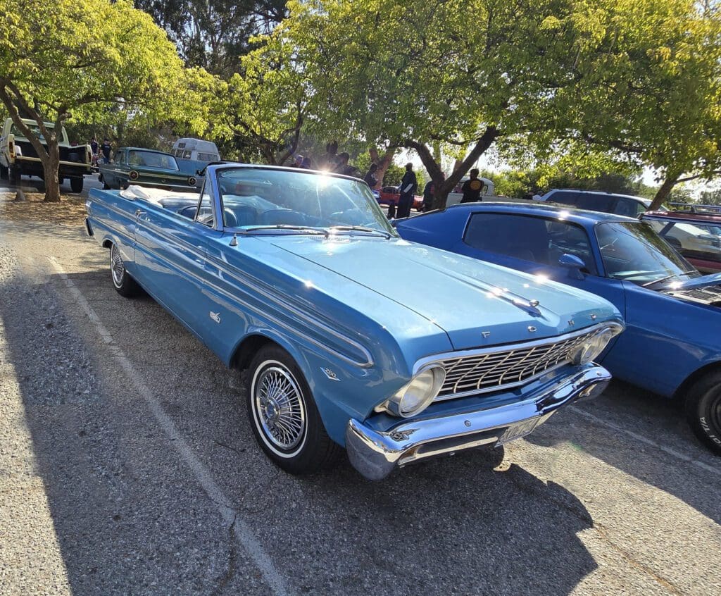 Classic blue vintage convertible parked under trees on a sunny day.
