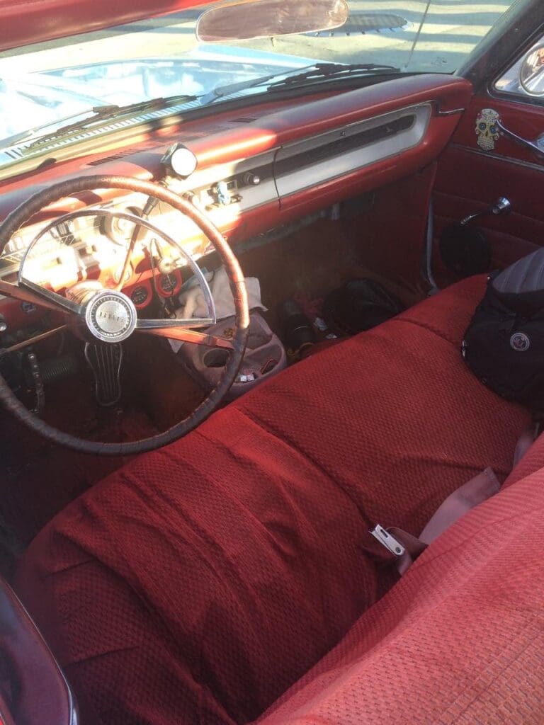 Interior of a vintage car with red upholstery and classic steering wheel.