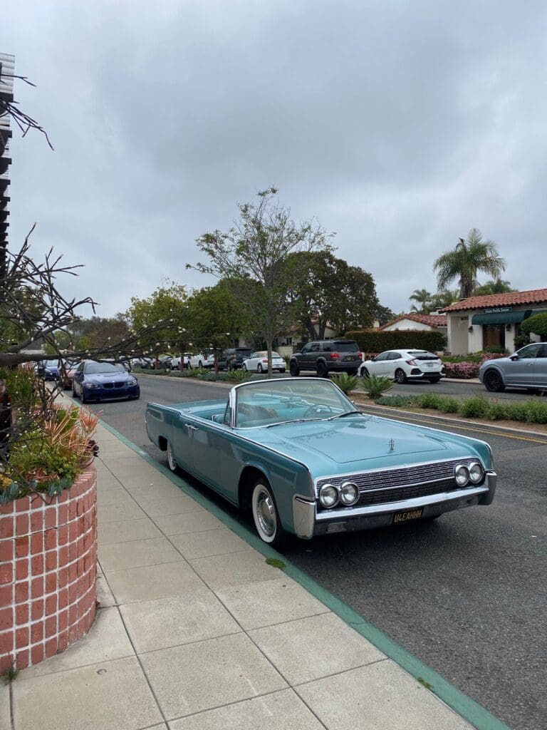 A vintage convertible car parked on a suburban street under cloudy skies.