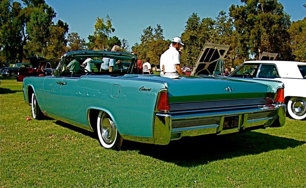 Vintage turquoise convertible car with passengers on a sunny day.